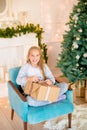 Little cute girl in pajamas near a Christmas tree with gifts and a bright fireplace decorated with garlands, needles and candles. Royalty Free Stock Photo