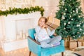 Little cute girl in pajamas near a Christmas tree with gifts and a bright fireplace decorated with garlands, needles and candles. Royalty Free Stock Photo