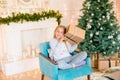 Little cute girl in pajamas near a Christmas tree with gifts and a bright fireplace decorated with garlands, needles and candles. Royalty Free Stock Photo