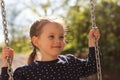 Little cute girl with pigtails smiling rides on a swing in polka dot clothes in the park