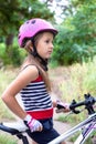 Little cute girl in a pink helmet near a bicycle