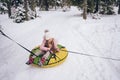 Little cute girl in pink warm outwear having fun rides inflatable snow tube in snowy white cold winter outdoors. Family sport Royalty Free Stock Photo