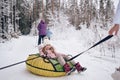 Little cute girl in pink warm outwear having fun rides inflatable snow tube in snowy white cold winter outdoors. Family sport Royalty Free Stock Photo