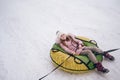 Little cute girl in pink warm outwear having fun rides inflatable snow tube in snowy white cold winter outdoors. Family sport Royalty Free Stock Photo