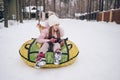 Little cute girl in pink warm outwear having fun rides inflatable snow tube in snowy white cold winter outdoors. Family sport Royalty Free Stock Photo