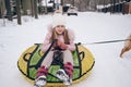 Little cute girl in pink warm outwear having fun rides inflatable snow tube in snowy white cold winter outdoors. Family sport Royalty Free Stock Photo