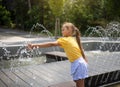 little cute girl playing with small fountains in the town square on a hot summer day