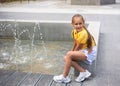 little cute girl playing with small fountains in the town square on a hot summer day