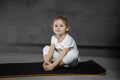 Little cute girl practicing yoga pose on grey background in dark room Royalty Free Stock Photo