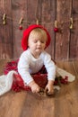 A little cute girl in a red plaid skirt and a red felt beret plays with cones and Christmas toys in a room decorated for Christmas