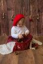 A little cute girl in a red plaid skirt and a red felt beret plays with cones and Christmas toys in a room decorated for Christmas Royalty Free Stock Photo