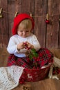 A little cute girl in a red plaid skirt and a red felt beret plays with cones and Christmas toys in a room decorated for Christmas Royalty Free Stock Photo