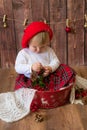 A little cute girl in a red plaid skirt and a red felt beret plays with cones and Christmas toys in a room decorated for Christmas Royalty Free Stock Photo