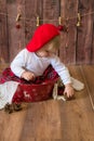 A little cute girl in a red plaid skirt and a red felt beret plays with cones and Christmas toys in a room decorated for Christmas