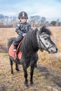 Little cute girl riding a little horse or pony in field in the winter Royalty Free Stock Photo