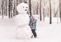 Little cute girl sculpts a big snowman in winter in the park Royalty Free Stock Photo