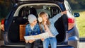 Agreeable boy and girl are looking at the road map while sitting in the auto`s trunk and discussing the move direction