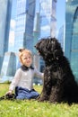 Little cute girl sits on grass with big black dog Royalty Free Stock Photo