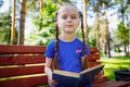 little cute girl is sitting on a bench and is reading a book Royalty Free Stock Photo