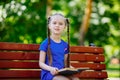 Little cute girl is sitting on a bench and is reading a book Royalty Free Stock Photo