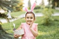 Little cute girl wear bunny ears holding basket with colorful painted eggs on Easter egg hunt in park