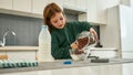 A little cute girl pouring cereal balls in a bowl with milk while in a big light kitchen Royalty Free Stock Photo