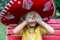 Little cute girl wearing a sombrero is covering her eyes with green dirty hands Royalty Free Stock Photo
