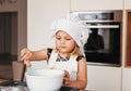 A little cute girl in a white chef`s hat makes dough in a white bowl Royalty Free Stock Photo