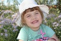 Little cute girl in white hat smiles near flowers Royalty Free Stock Photo