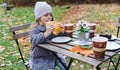 Little cute girls, sisters in coats seat, eat buns, drink coffee in cafe in autumn park. Cozy wooden table, chairs. Drinks,food to Royalty Free Stock Photo