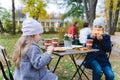 Little cute girls, sisters in coats seat, eat buns, drink coffee in cafe in autumn park. Cozy wooden table, chairs. Drinks,food to Royalty Free Stock Photo