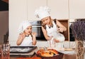 Little cute girls sisters in white chef hats bake buns in the kitchen
