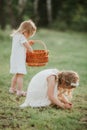 Little cute girls in white dresses with baskets collect cones on a sunny day in the park