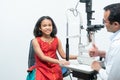 little cute Indian girl child patient is getting eyes exam from professional ophthalmologist or optometrist man at clinic Royalty Free Stock Photo