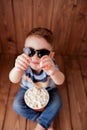 Little cute kid baby boy 2-3 years old , 3d cinema glasses holding bucket for popcorn, eating fast food on wooden background. Kids Royalty Free Stock Photo