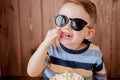 Little cute kid baby boy 2-3 years old , 3d imax cinema glasses holding bucket for popcorn, eating fast food on wooden background Royalty Free Stock Photo