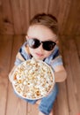 Little cute kid baby boy 2-3 years old , 3d imax cinema glasses holding bucket for popcorn, eating fast food on wooden background Royalty Free Stock Photo