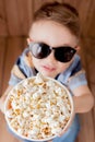 Little cute kid baby boy 2-3 years old , 3d imax cinema glasses holding bucket for popcorn, eating fast food on wooden background Royalty Free Stock Photo