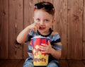 Little cute kid baby boy 2-3 years old , 3d imax cinema glasses holding bucket for popcorn, eating fast food on wooden background Royalty Free Stock Photo