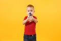 Little cute kid baby boy 3-4 years old, football fan in red t-shirt holding in hand pipe, blowing isolated on yellow Royalty Free Stock Photo