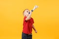 Little cute kid baby boy 3-4 years old, football fan in red t-shirt holding in hand pipe, blowing isolated on yellow Royalty Free Stock Photo