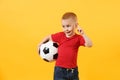 Little cute kid baby boy 3-4 years old, football fan in red t-shirt holding in hand soccer ball isolated on yellow Royalty Free Stock Photo