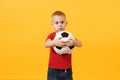 Little cute kid baby boy 3-4 years old, football fan in red t-shirt holding in hand soccer ball isolated on yellow Royalty Free Stock Photo