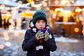 Little cute kid boy drinking hot children punch or chocolate on German Christmas market. Happy child on traditional Royalty Free Stock Photo