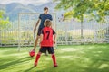 Little cute kid boy in red football uniform and his trainer or father playing soccer, football on field, outdoors Royalty Free Stock Photo