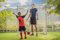 Little cute kid boy in red football uniform and his trainer or father playing soccer, football on field, outdoors Royalty Free Stock Photo