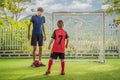 Little cute kid boy in red football uniform and his trainer or father playing soccer, football on field, outdoors Royalty Free Stock Photo