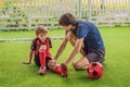 Little cute kid boy in red football uniform and his trainer or father playing soccer, football on field, outdoors Royalty Free Stock Photo