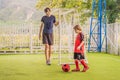 Little cute kid boy in red football uniform and his trainer or father playing soccer, football on field, outdoors Royalty Free Stock Photo