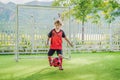 Little cute kid boy in red football uniform playing soccer, football on field, outdoors. Active child making sports with Royalty Free Stock Photo